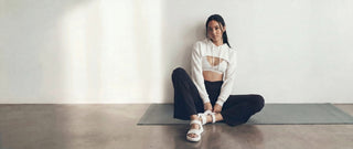 Woman in cropped hoodie sitting on yoga mat in studio. 