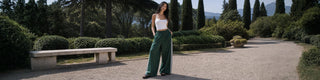 woman standing in park setting wearing green track pants and a white tank