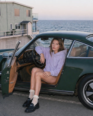 Woman sitting in a vintage green car by the ocean with houses in the background